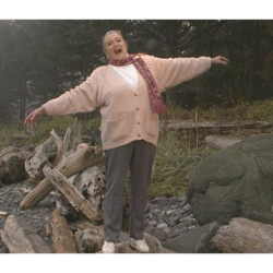 Marie Rackham standing on a driftwood log, arms joyfully outstretched.