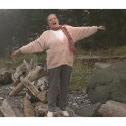 Marie Rackham standing on a driftwood log, arms joyfully outstretched.